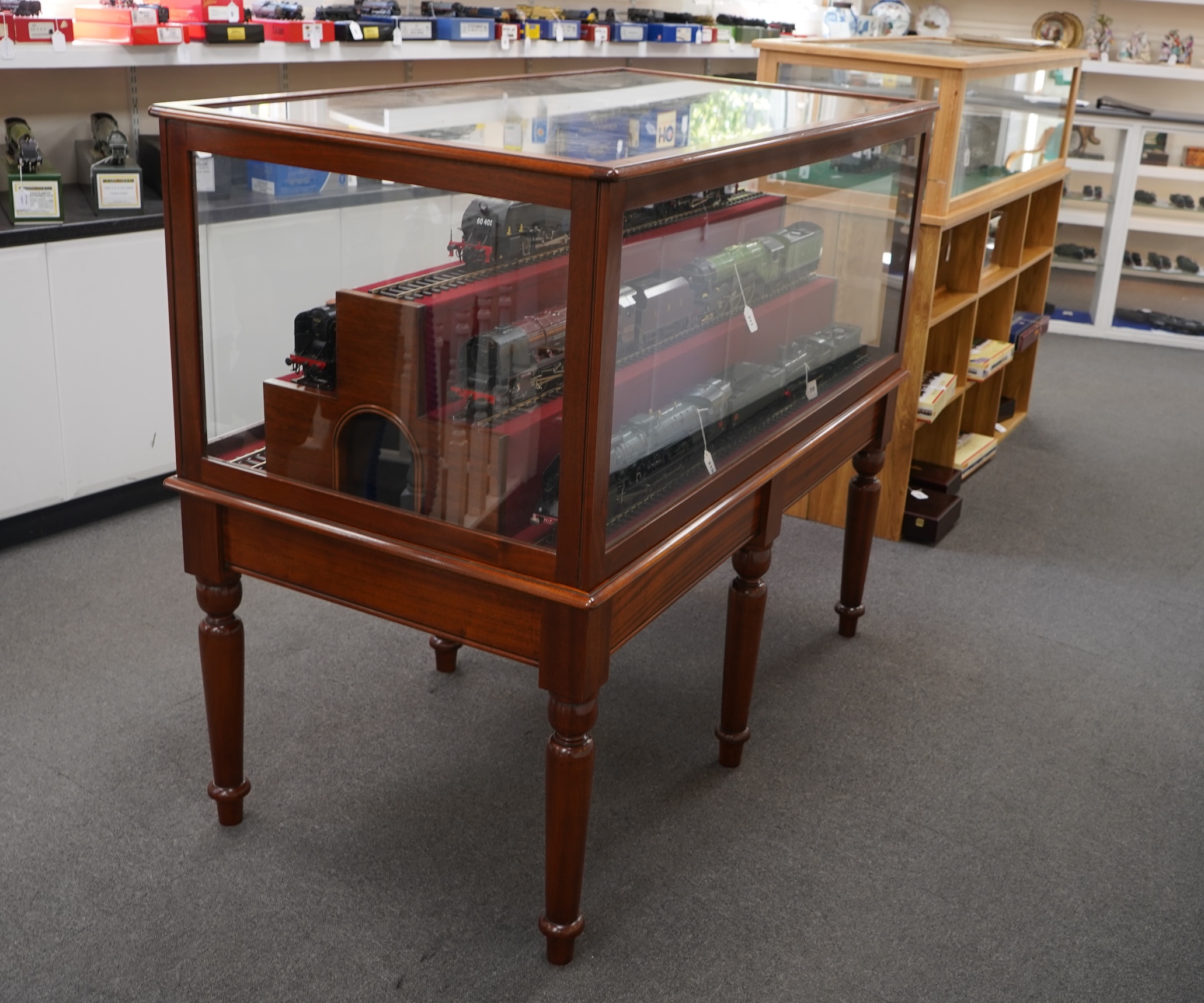 A substantial tiered display cabinet in a mahogany-tinted hardwood, with a lift off glazed cover, intended for Gauge One model railway rolling stock, currently fitted with five lengths of 45mm display railway track, dime